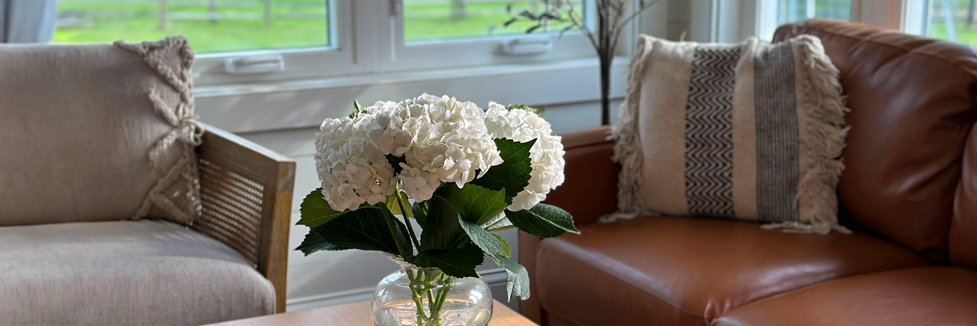 Bright white hydrangeas in a vase on a coffee table, surrounded by cozy armchairs and natural light.
