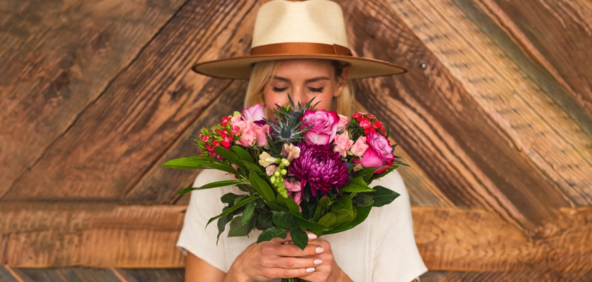 A woman wearing a stylish hat holds a vibrant floral bouquet, radiating joy and beauty.