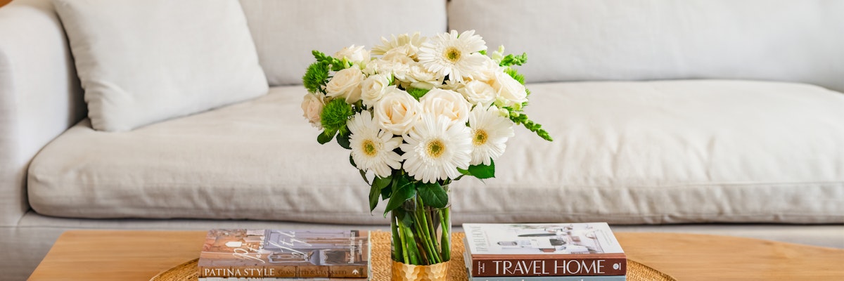 Elegant white gerbera daisies and roses in a stylish vase on a wooden table.