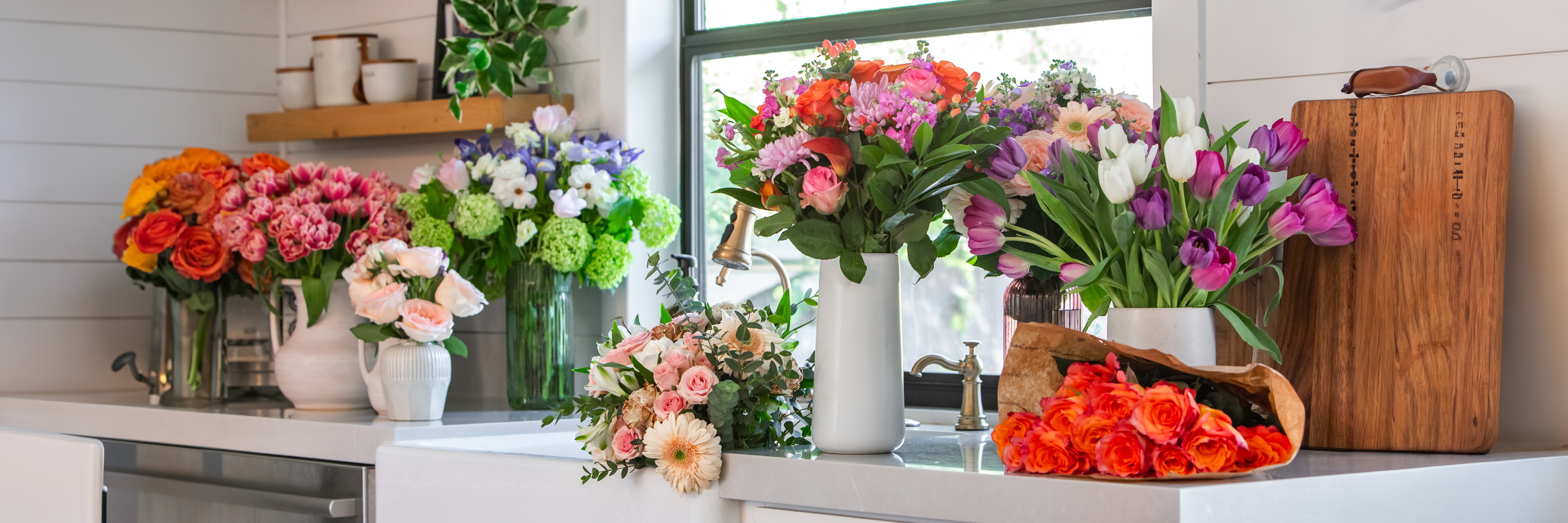 Vibrant floral arrangements in a sunlit kitchen, featuring roses, tulips, and mixed blooms.