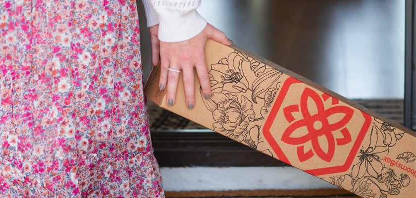 A person in a floral dress holds a stylish floral subscription box at home.