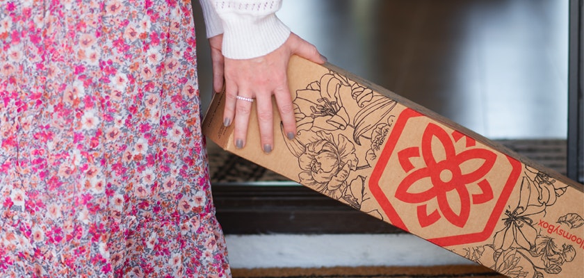 A person in a floral dress holds a stylish floral subscription box at home.