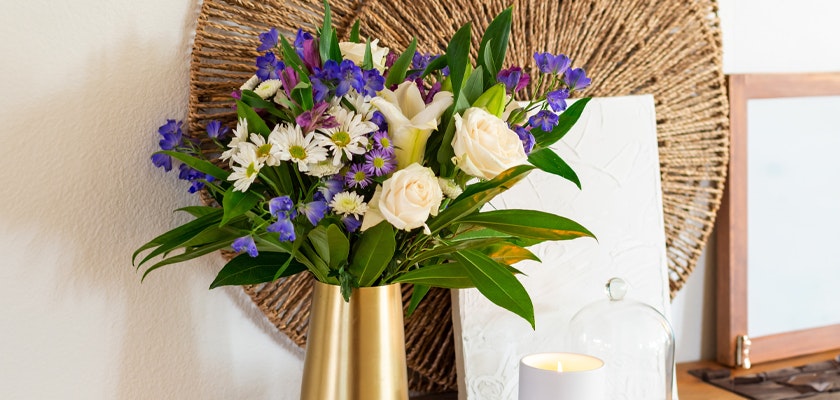 Charming floral arrangement featuring white roses, purple blooms, and greenery in a stylish vase.