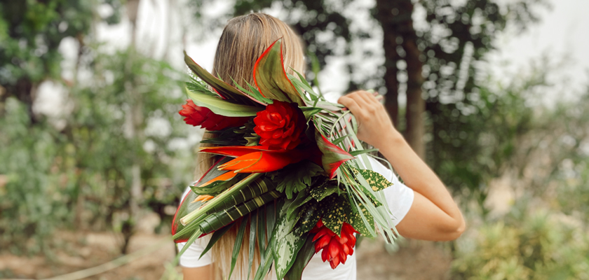 A vibrant tropical floral arrangement featuring red blooms and lush green leaves, held by a woman.