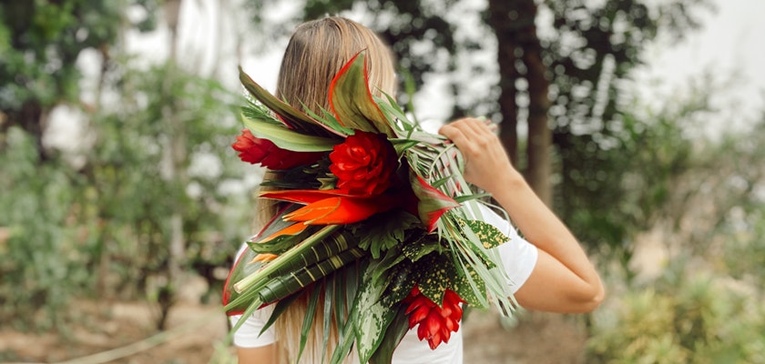 A vibrant tropical floral arrangement featuring red blooms and lush green leaves, held by a woman.