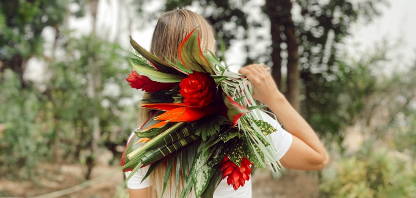 A vibrant tropical floral arrangement featuring red blooms and lush green leaves, held by a woman.