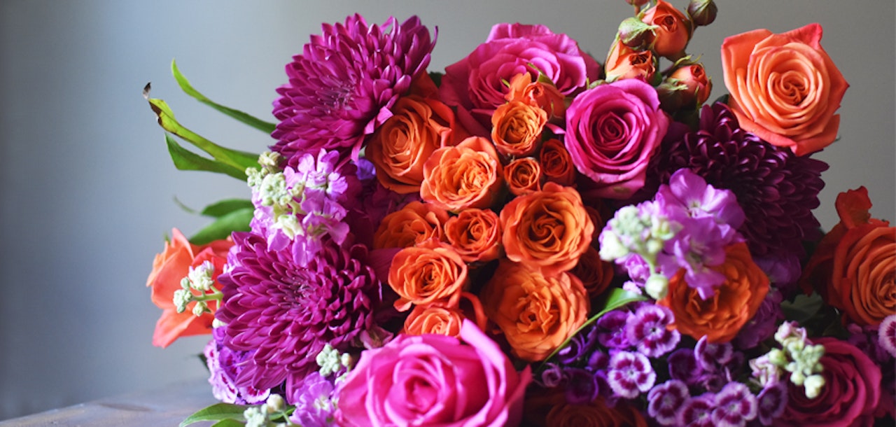 Vibrant bouquet featuring orange and pink roses, purple dahlias, and colorful blooms for any celebration.