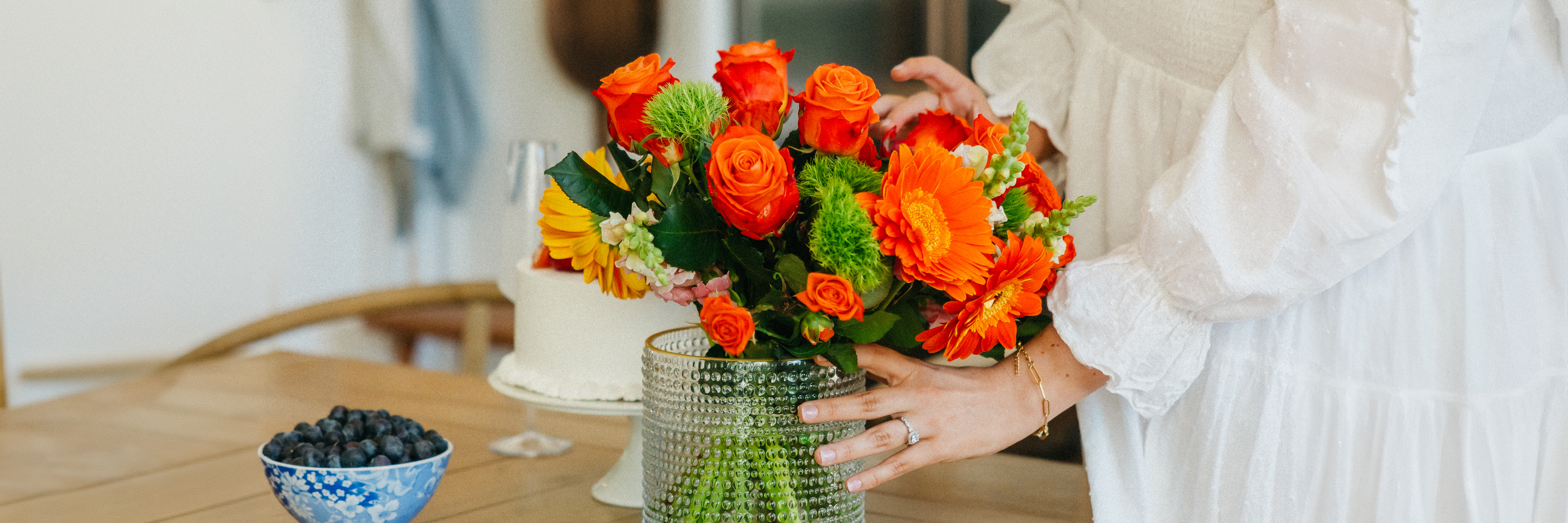A vibrant floral arrangement featuring orange roses and cheerful blooms in a stylish glass vase.