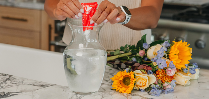 A person adds floral preservative to water in a vase for a vibrant bouquet arrangement.