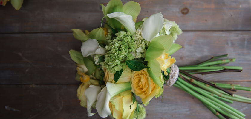 Delicate bouquet featuring yellow roses, white calla lilies, and lush greenery, elegantly arranged.
