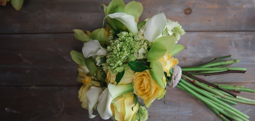 Delicate bouquet featuring yellow roses, white calla lilies, and lush greenery, elegantly arranged.