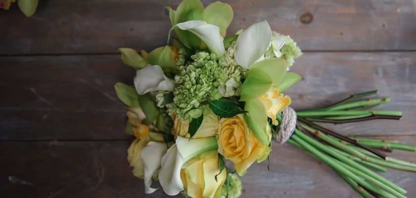 Delicate bouquet featuring yellow roses, white calla lilies, and lush greenery, elegantly arranged.
