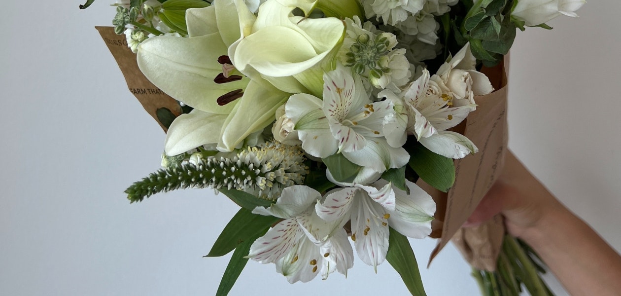 Elegant white floral bouquet featuring lilies, alstroemeria, and greenery, held by a hand.