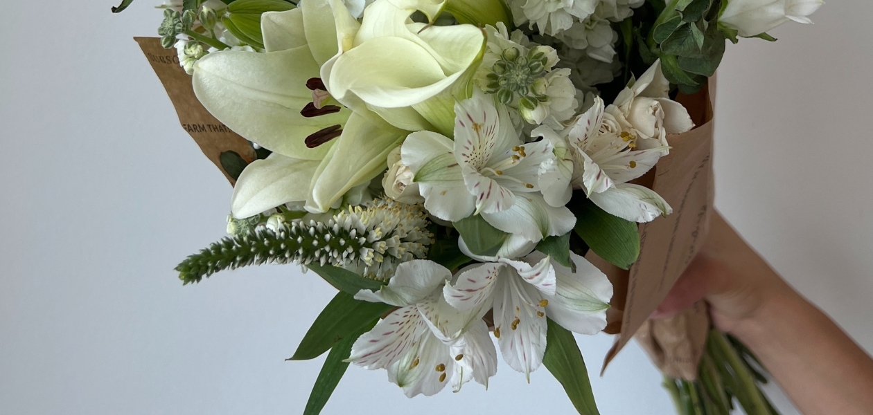 Elegant white floral bouquet featuring lilies, alstroemeria, and greenery, held by a hand.