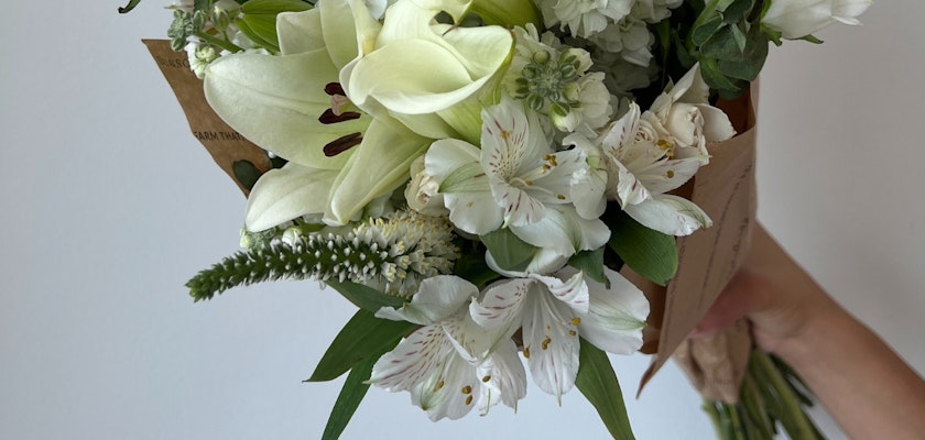 Elegant white floral bouquet featuring lilies, alstroemeria, and greenery, held by a hand.