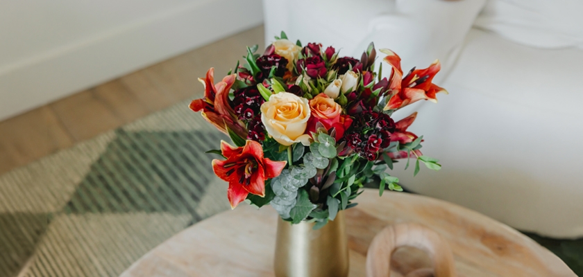 Vibrant floral arrangement featuring roses, lilies, and greenery in an elegant gold vase.