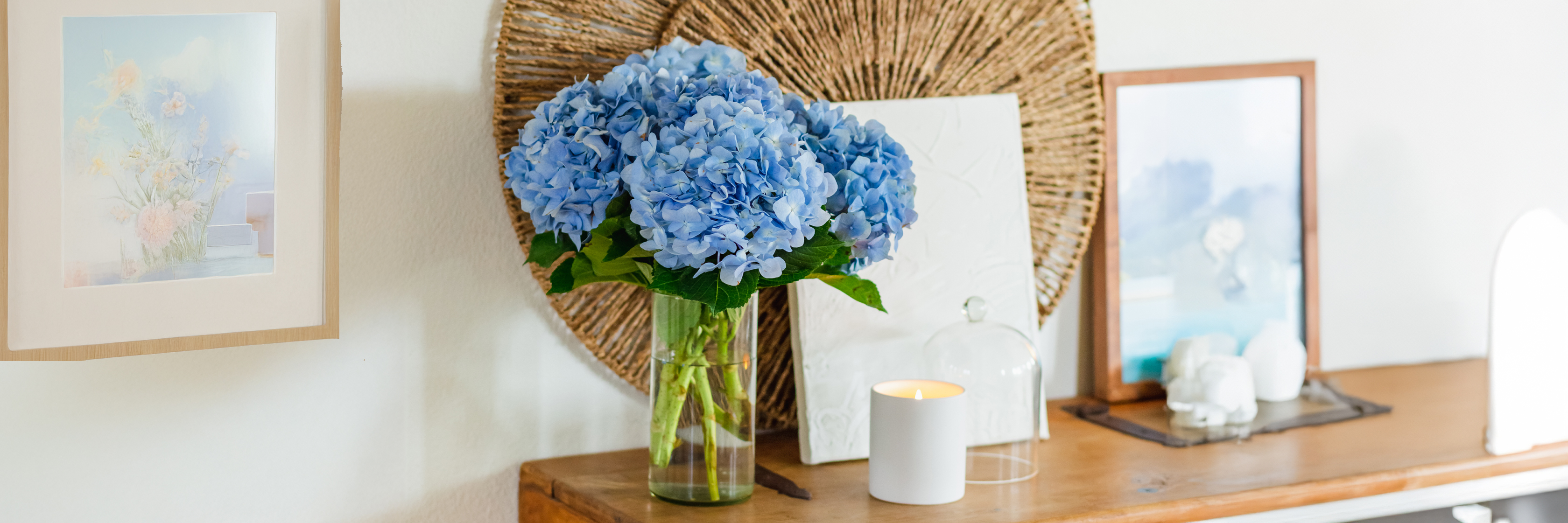 A vibrant bouquet of blue hydrangeas in a vase on a wooden table, complemented by decorative art.