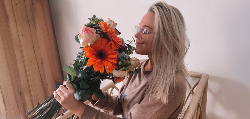 Young woman holding a vibrant bouquet of orange gerberas and pink roses, exuding cheerful vibes.