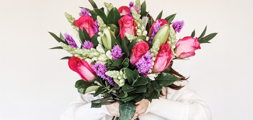 A vibrant bouquet featuring pink roses, purple blooms, and lush greenery in full display.