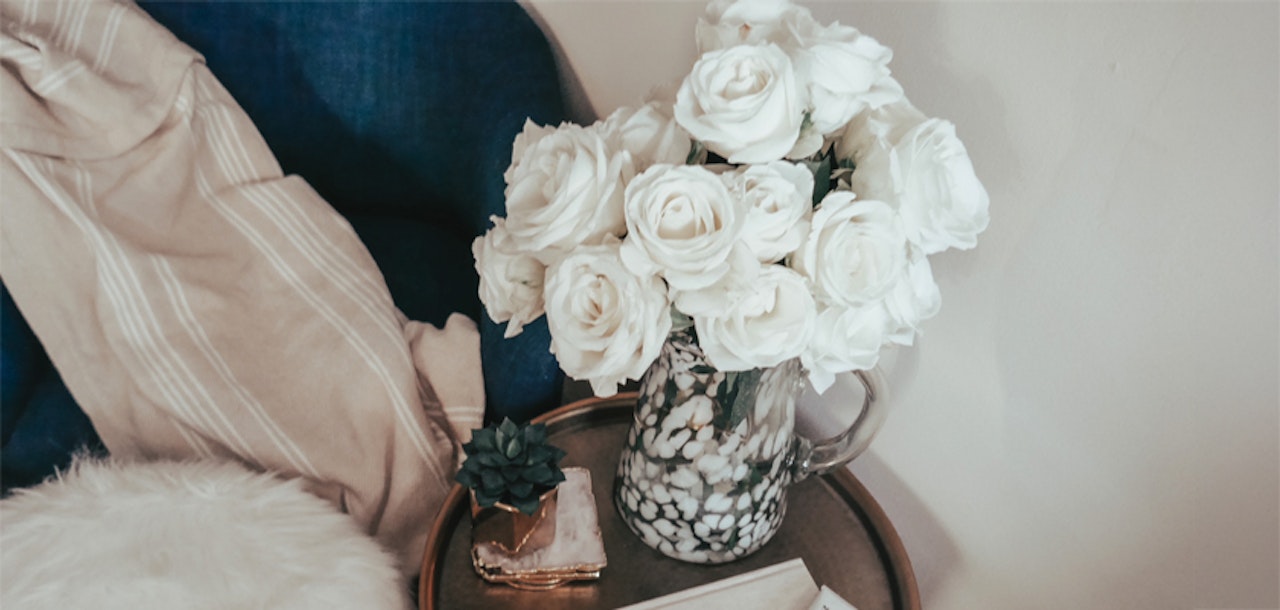 A charming arrangement of white roses in a decorative vase, set on a cozy table with soft textures.
