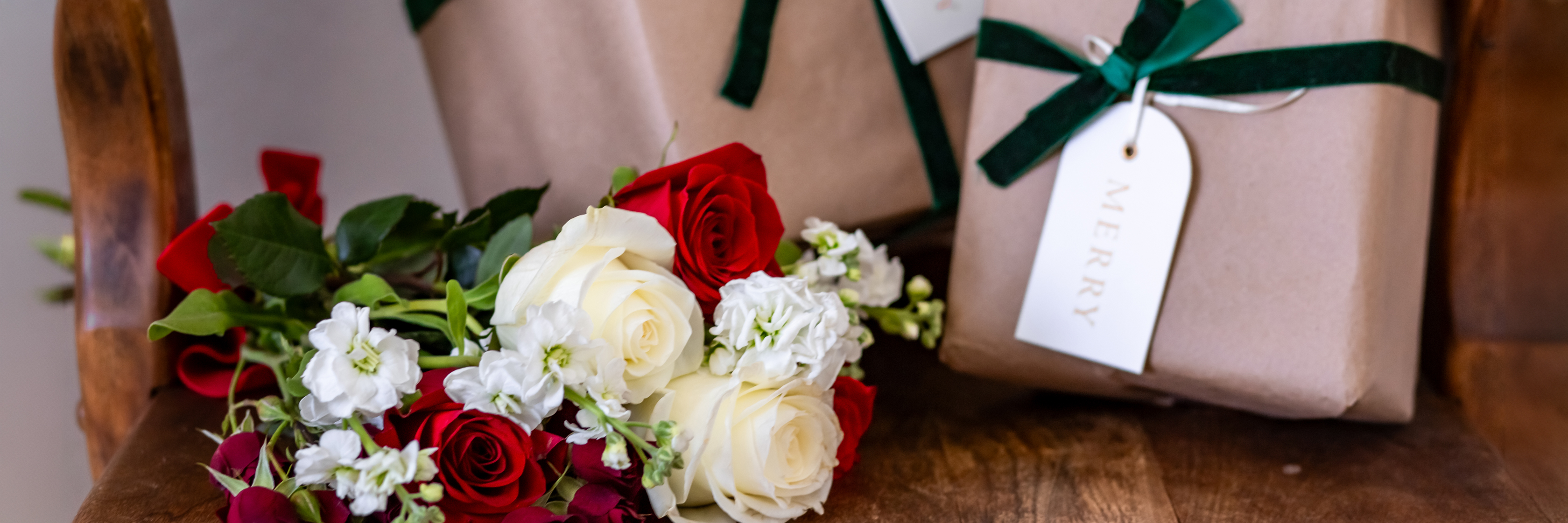 Elegant gift packages tied with green ribbons alongside a charming bouquet of red and white roses.