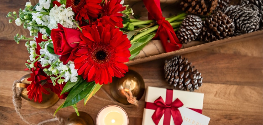 Vibrant red gerbera daisies and roses alongside festive decor, perfect for holiday celebrations.