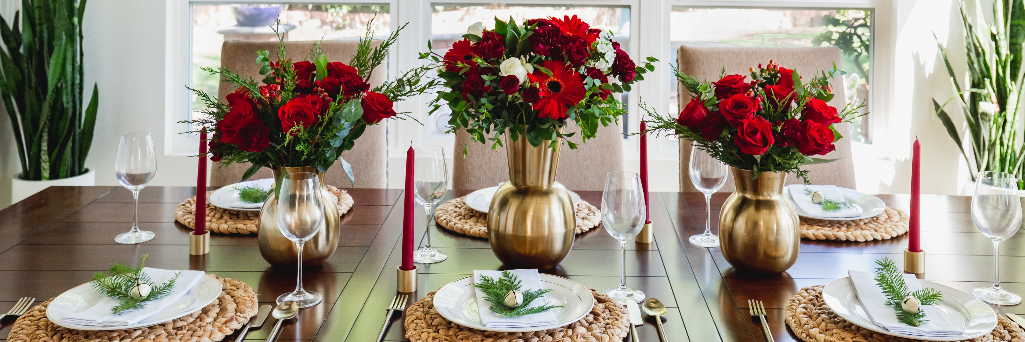 Elegant dining table adorned with vibrant red flower arrangements, candles, and festive decor.