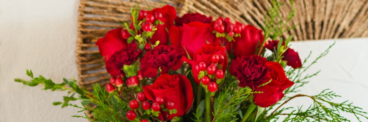 Vibrant arrangement of red roses and deep red carnations with seasonal greenery.