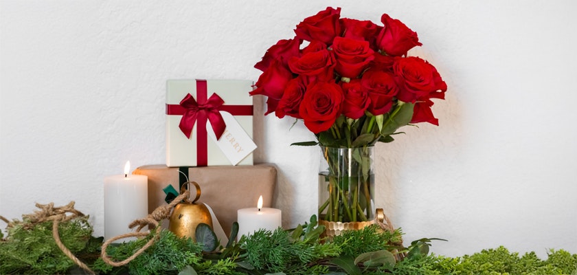 Elegant red roses in a glass vase, accompanied by gifts and candles, perfect for celebrations.