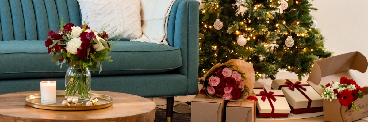 Cozy living room scene featuring a decorated Christmas tree, gifts, and floral arrangements.