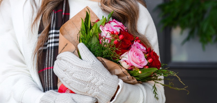 A cozy winter scene featuring a woman holding a vibrant floral bouquet with festive colors.
