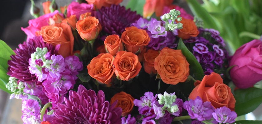 Vibrant floral arrangement featuring orange roses, purple chrysanthemums, and pink blooms.