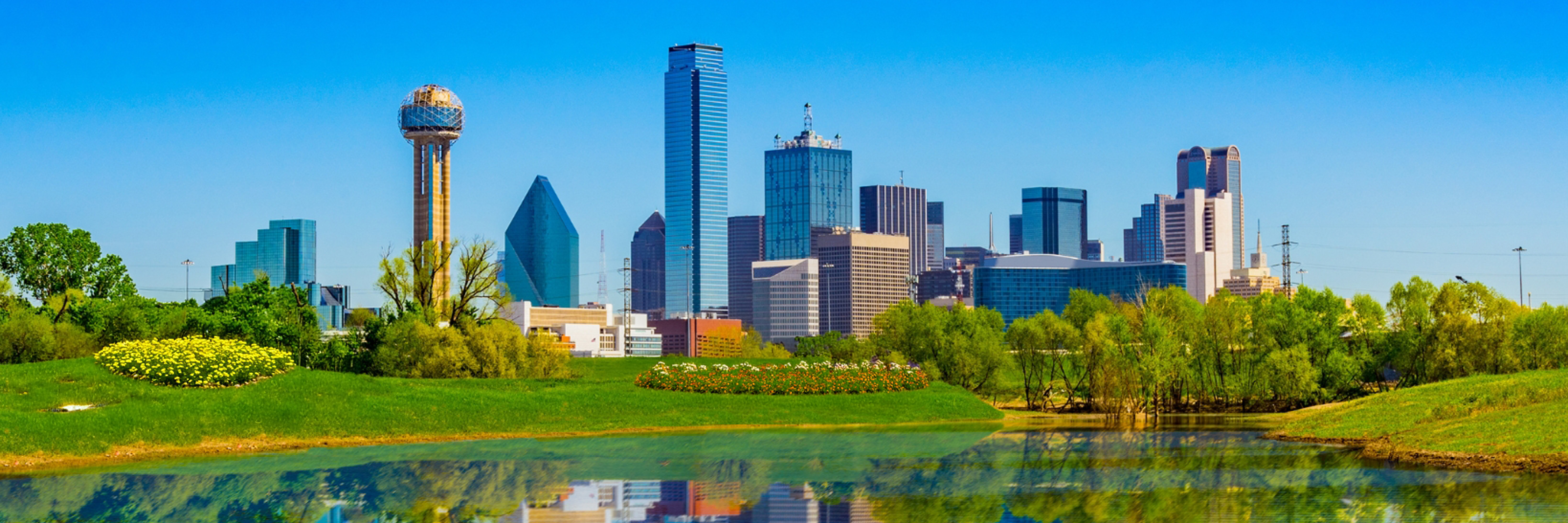 Vibrant Dallas skyline reflected on a serene lake under a clear blue sky.