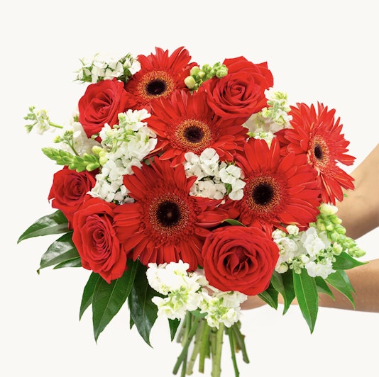 Vibrant bouquet featuring red roses and gerbera daisies, accented with white florals.