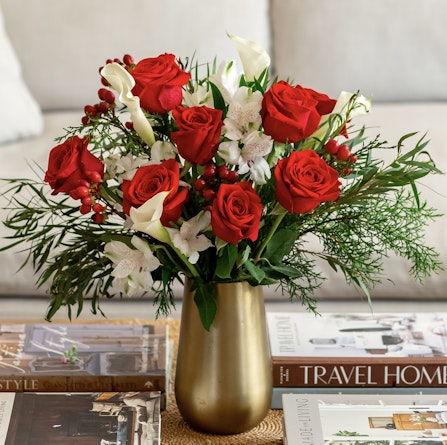 Elegant arrangement of red roses, white blooms, and greenery in a stylish gold vase.