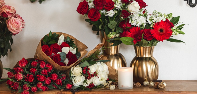 Vibrant assortment of red and white flowers in elegant vases, complemented by a cozy candle.