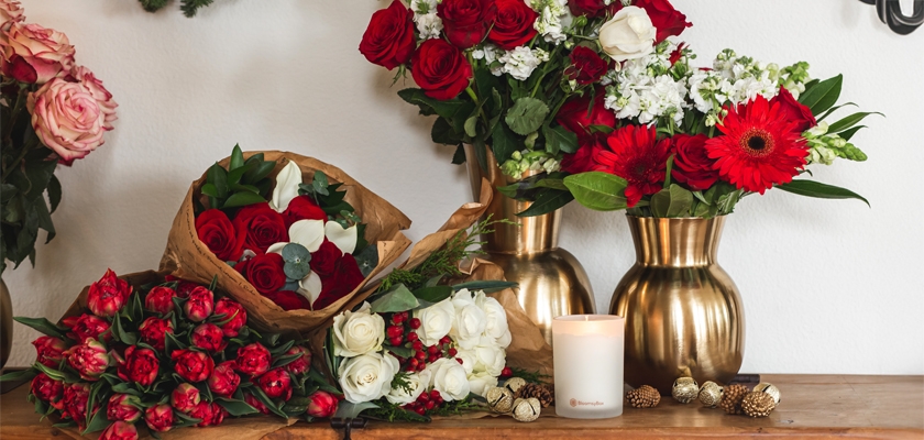 Vibrant assortment of red and white flowers in elegant vases, complemented by a cozy candle.