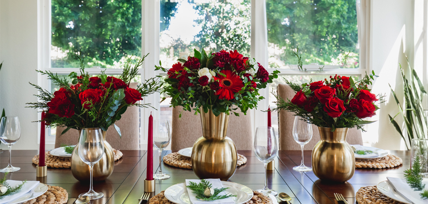 Elegant table setting featuring vibrant red floral arrangements and candles for festive gatherings.