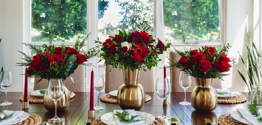 Elegant table setting featuring vibrant red floral arrangements and candles for festive gatherings.