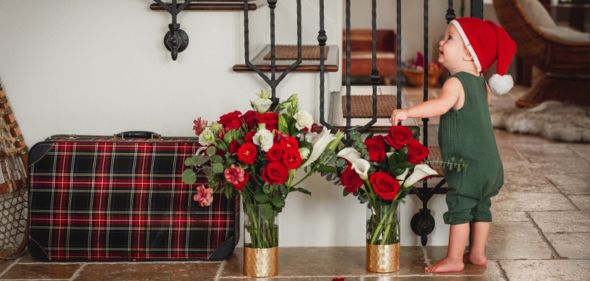 A cheerful child wearing a Santa hat beside beautiful red and white floral arrangements.
