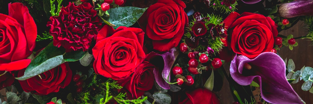 Lush red roses and deep purple calla lilies arranged elegantly with greenery and berries.