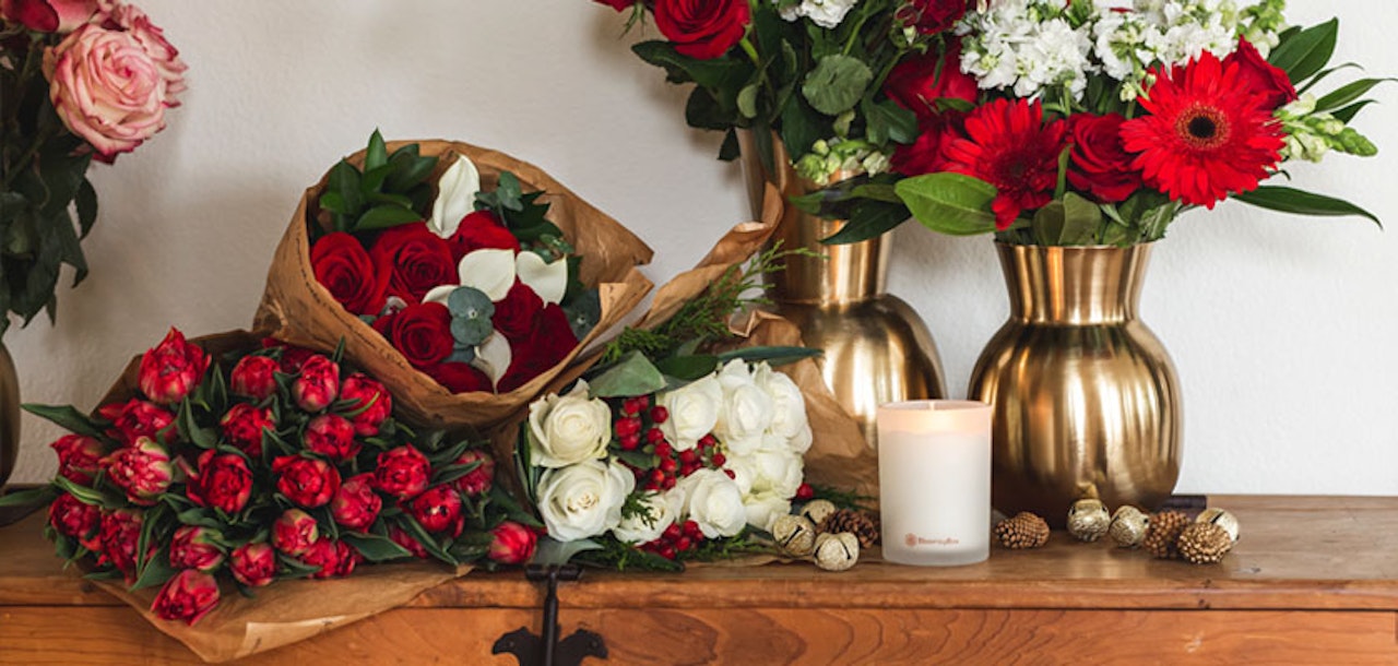 Vibrant floral display featuring red roses, white flowers, and elegant vases on a rustic wooden surface.