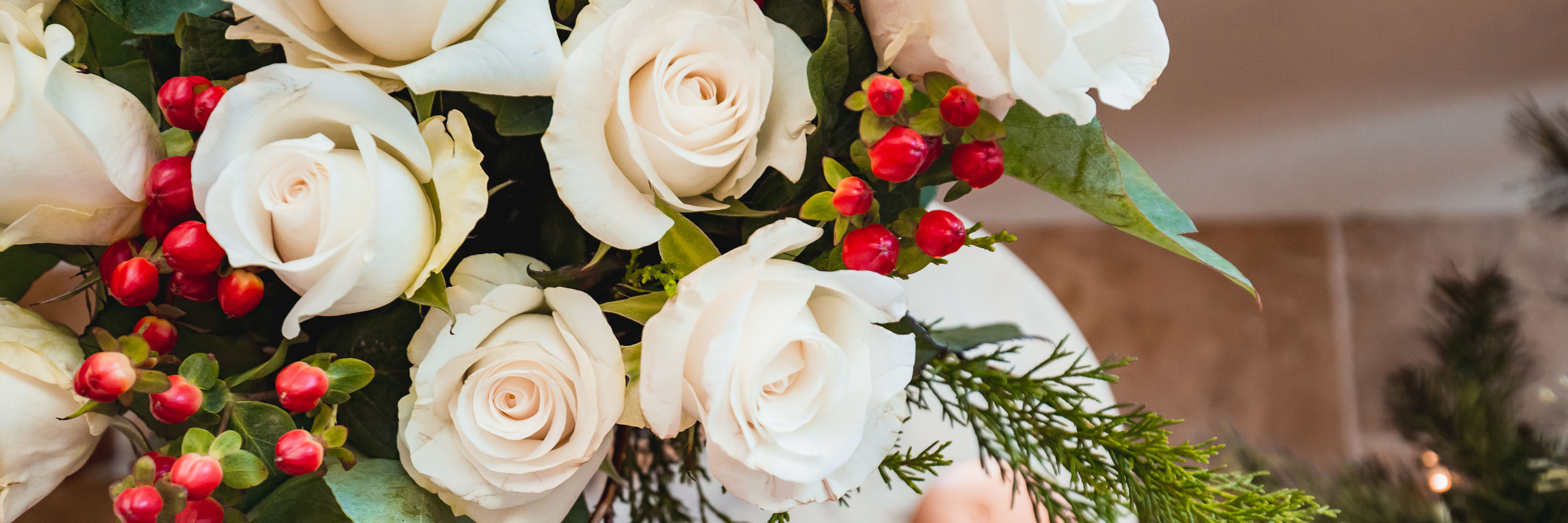 Elegantly arranged white roses adorned with red berries and greenery, perfect for festive occasions.