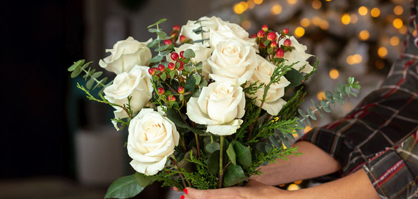 Elegant white roses complemented by greenery and red berries, ideal for festive occasions.