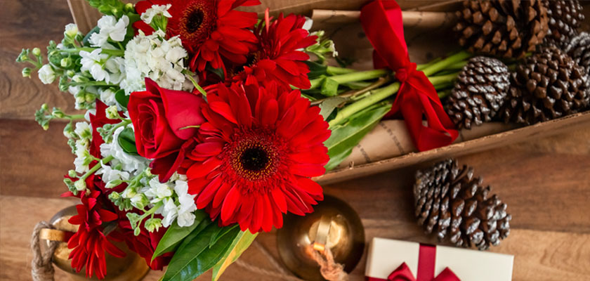 Vibrant red gerbera daisies and roses arranged elegantly with greenery, perfect for celebrations.