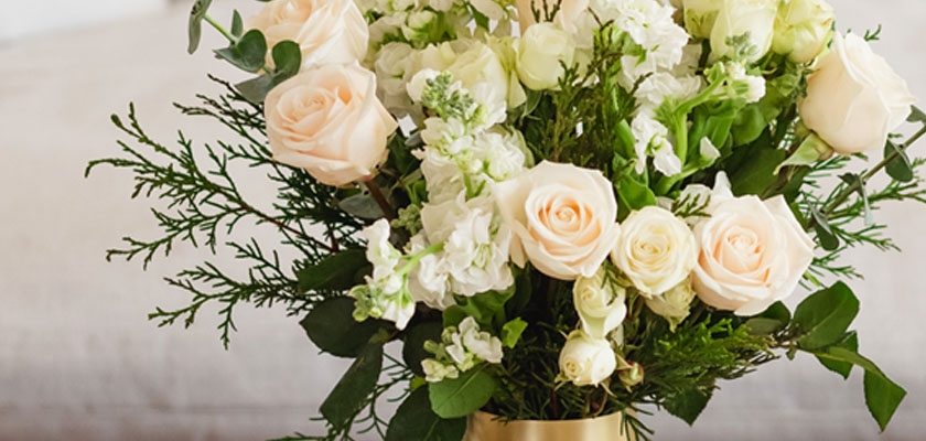 Elegant floral arrangement featuring soft peach roses and white blooms set in a chic gold vase.