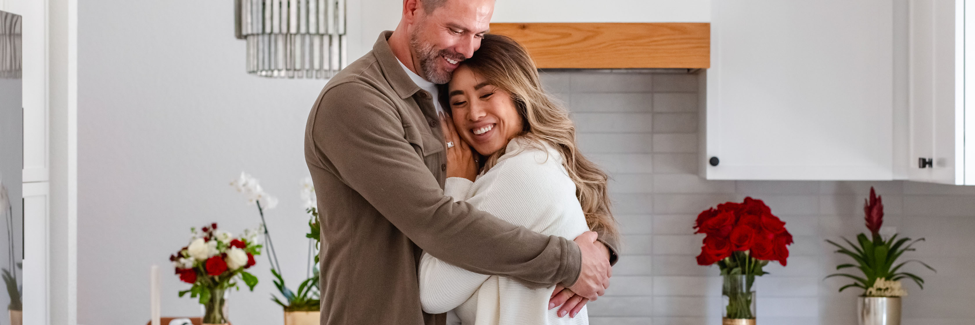 A joyful couple embracing in a modern kitchen adorned with vibrant floral arrangements.