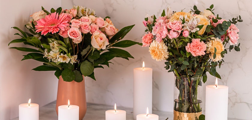 Elegant floral arrangements featuring pink roses, gerberas, and candles on a marble surface.