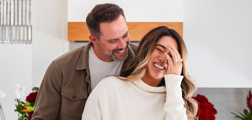 A joyful couple shares a moment together in a bright kitchen, surrounded by vibrant flowers.