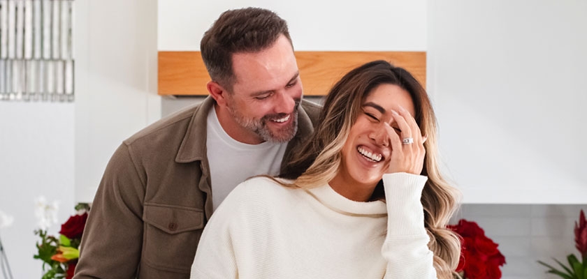 A joyful couple shares a moment together in a bright kitchen, surrounded by vibrant flowers.